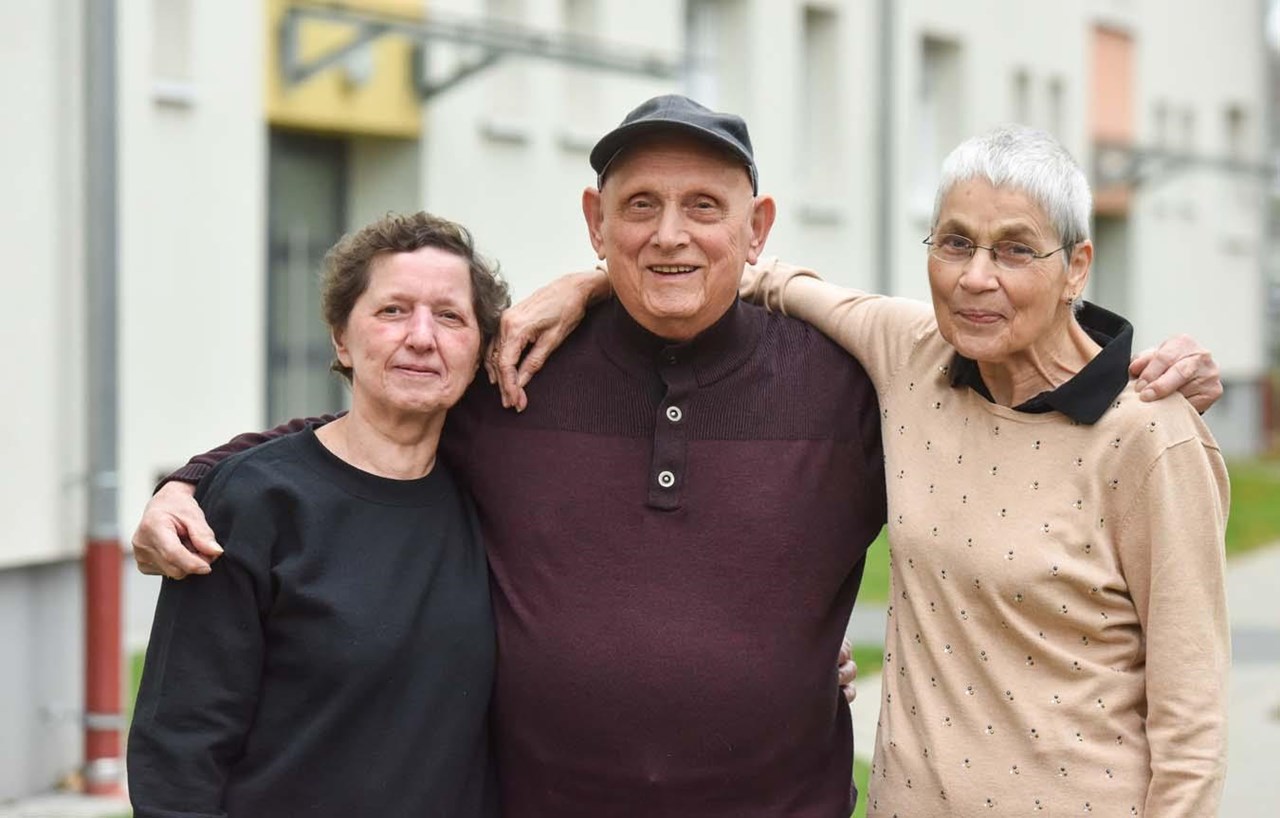 Zwei ältere Frauen und ein älterer Mann blicken Arm in Arm in die Kamera