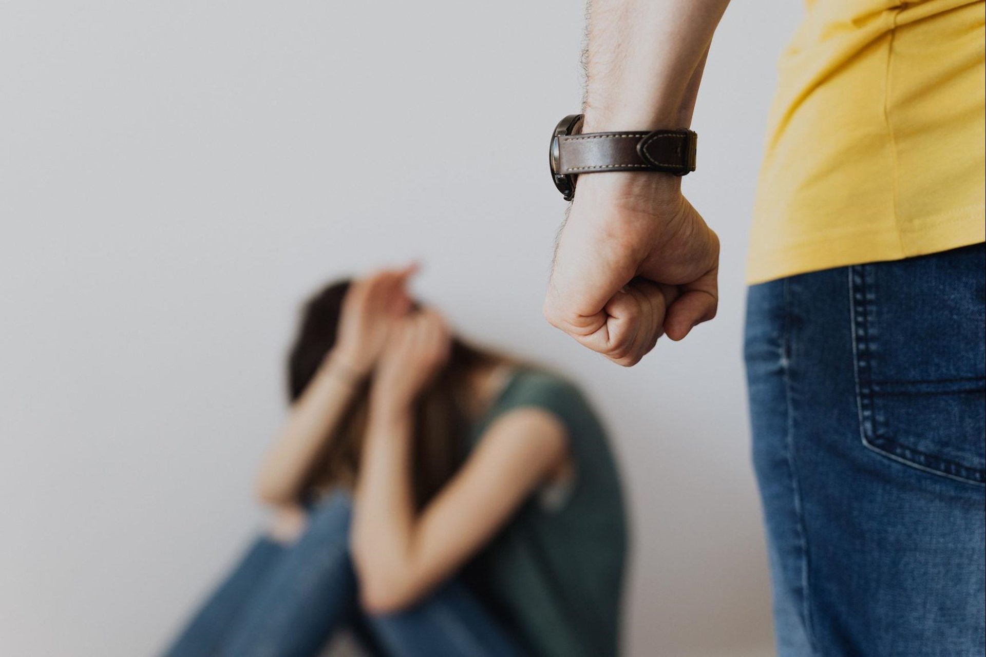 Eine Frau duckt sich am Boden und man sieht im Anschnitt die geballte Hand eines Mannes im Vordergrund.