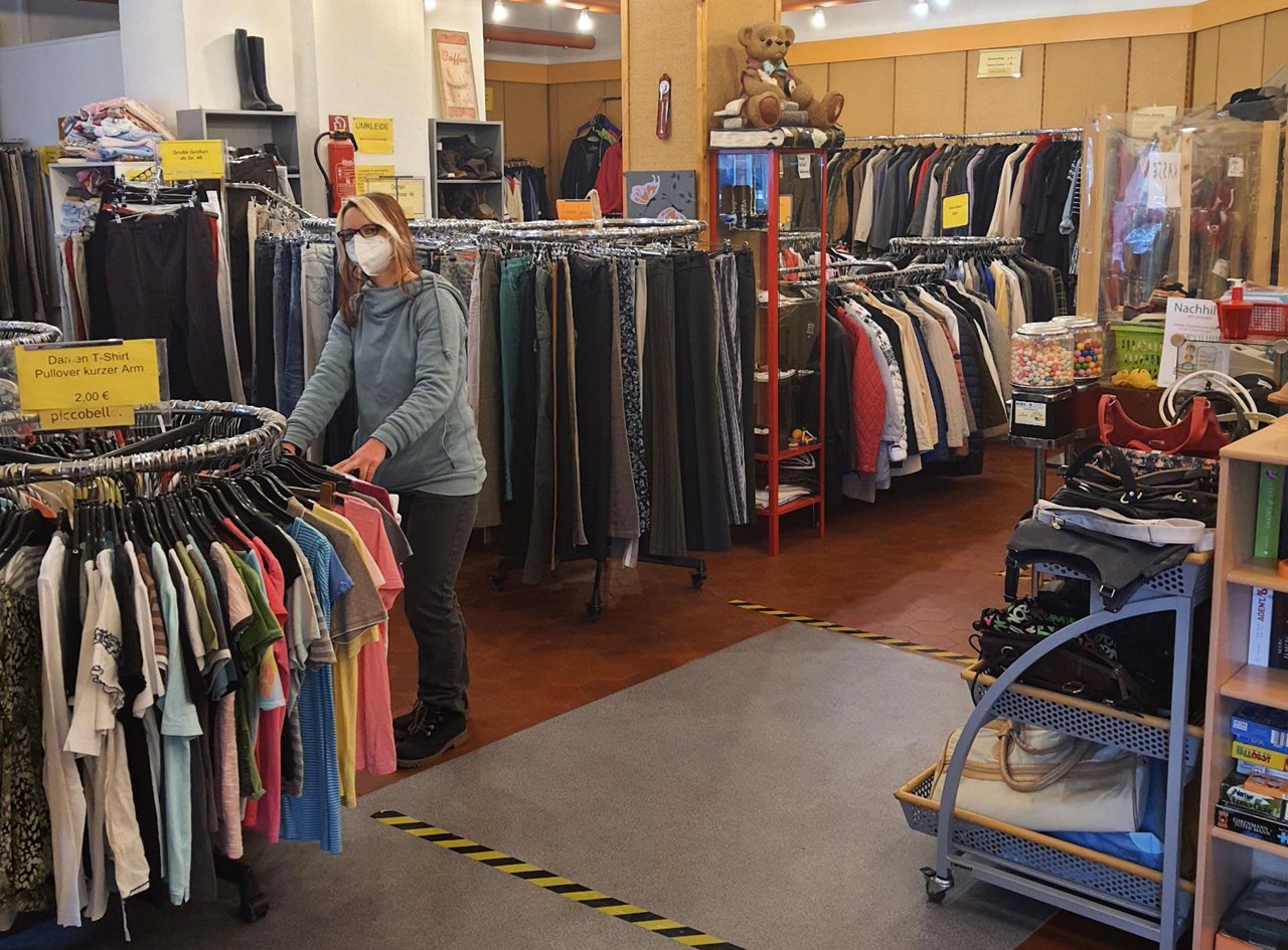 Eine junge Frau schaut sich geschützt mit einer FFP2-Maske im Second-Hand-Laden Piccobello Kleidung an.