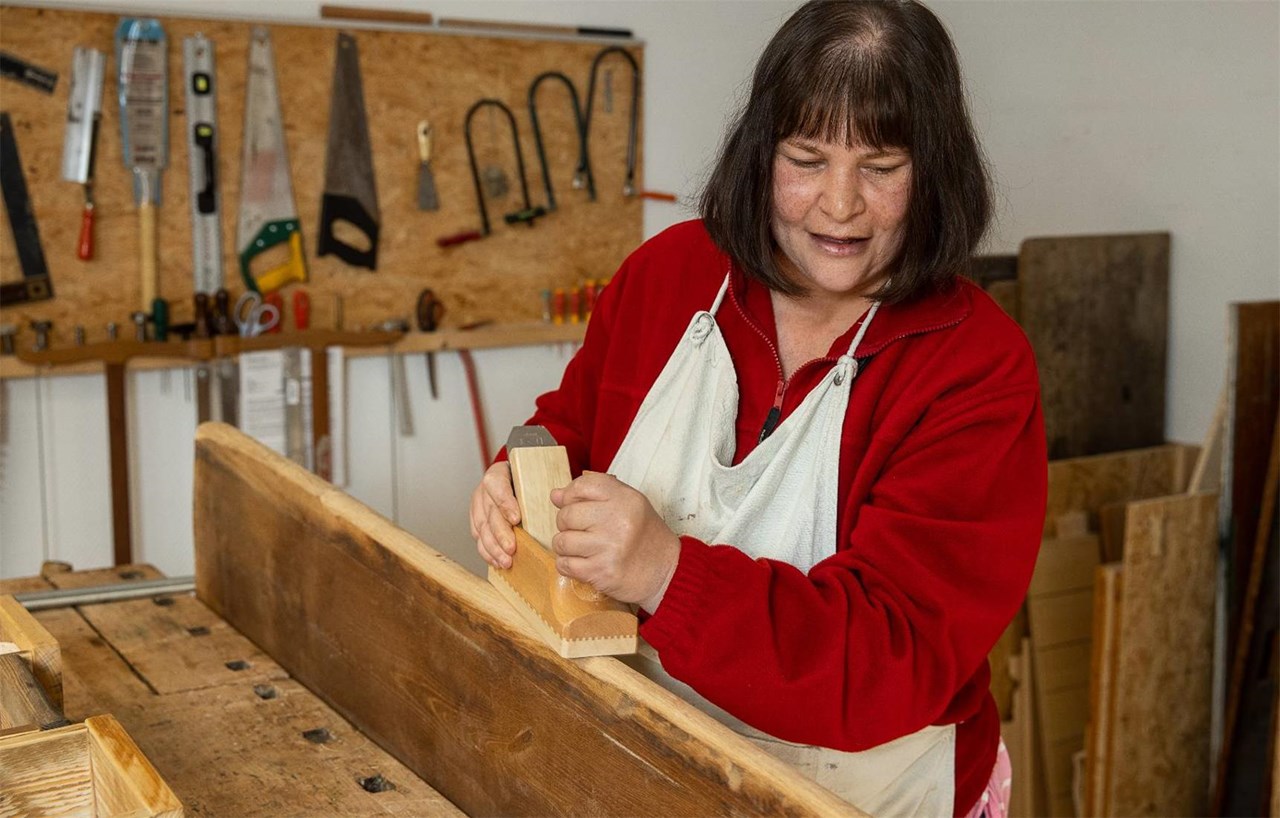 Eine Frau arbeitet mit einem Hobel in der Ergotherapie-Werkstatt.