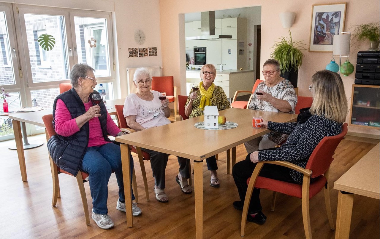 Senior*innen sitzen zusammen mit einer Betreuerinnen im Gruppenraum einer Wohngemeinschaft im Rohlandshof.