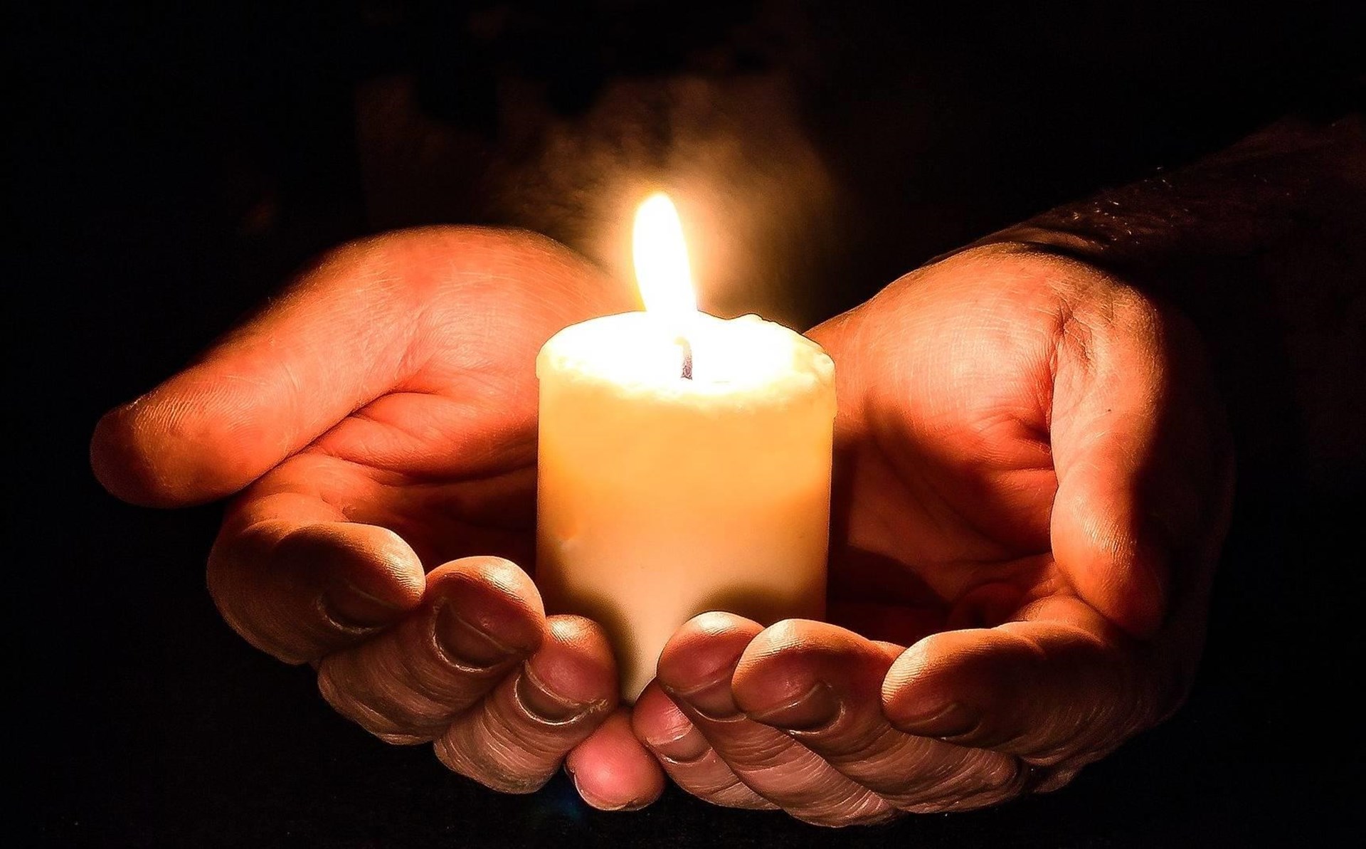 Hände, zu einer Schale geformt, halten eine kleine weiße Kerze
